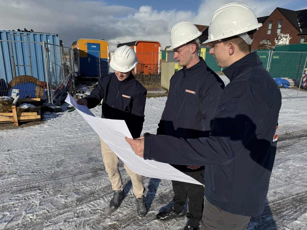 Drie medewerkers van Bouwsector Nederland met witte helm bekijken een bouwtekening op een besneeuwd bouwterrein